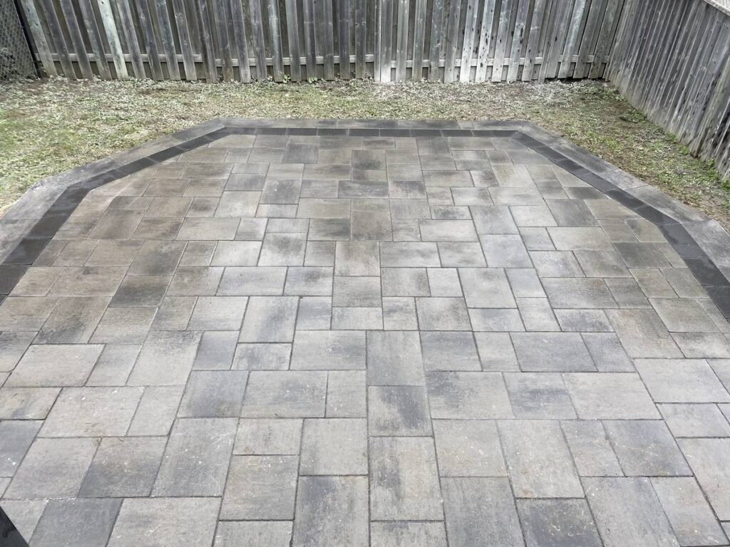 Square interlocking patio with a charcoal border in a fenced backyard