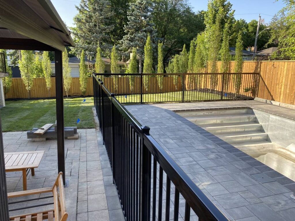 Grey interlocking pool deck with black pool fence in North York